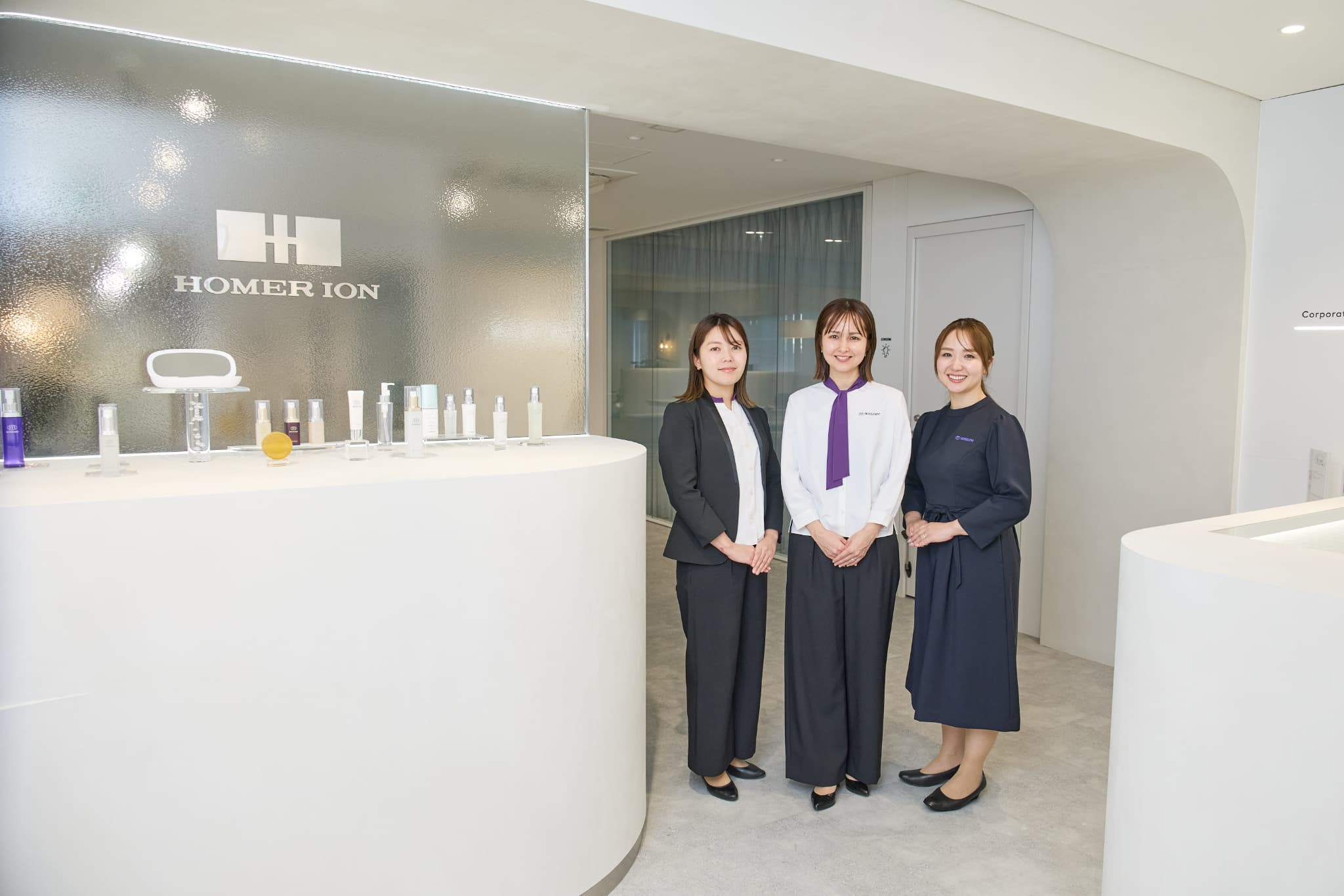 ホーマーイオンのスタッフユニフォームを着用した女性。白を基調に紫をワンポイントにしたブラウスに、黒のジャケットを着用。