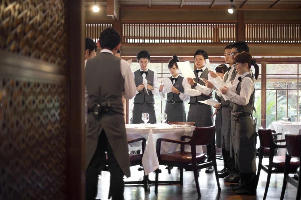 白いシャツとグレーのベスト、パンツの制服を着用したレストランスタッフが打ち合わせをしている様子