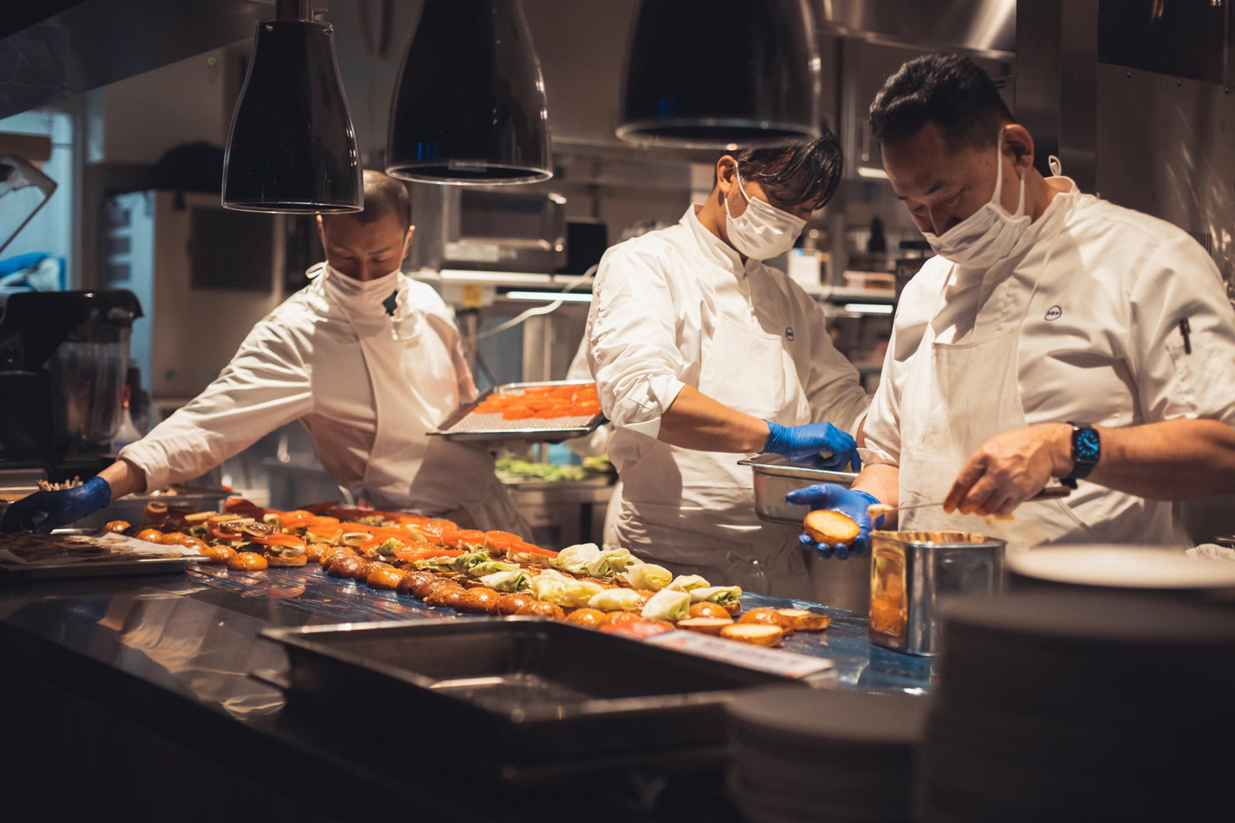 白いコックコートを着用した男性スタッフ3名が調理する様子
