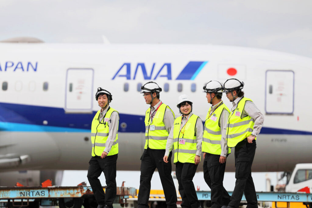 グレー、蛍光イエローの作業服とヘルメットを着用した整備スタッフ5名